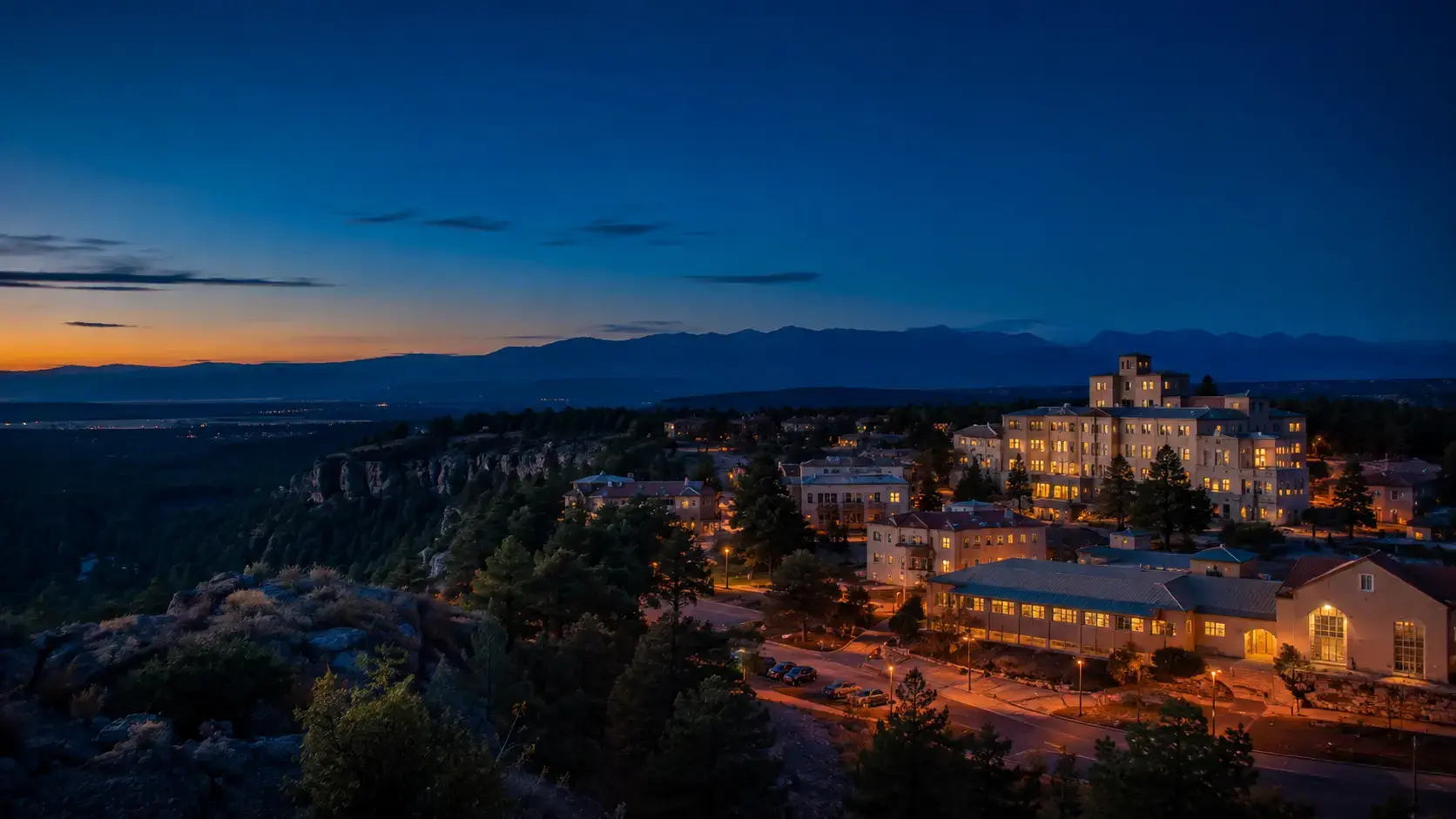 Los Alamos, New Mexico, at blue hour with warm lights across the mesa and mountains beyond.