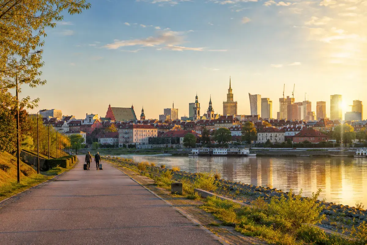 Warsaw at sunrise from the Vistula riverbank as travelers begin their departure day.
