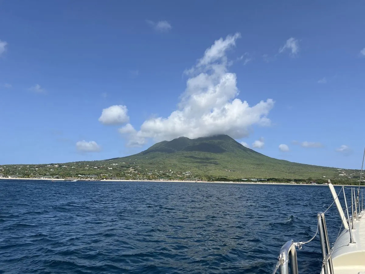 Approaching the green coastline of Nevis by boat, with Nevis Peak rising into the clouds.