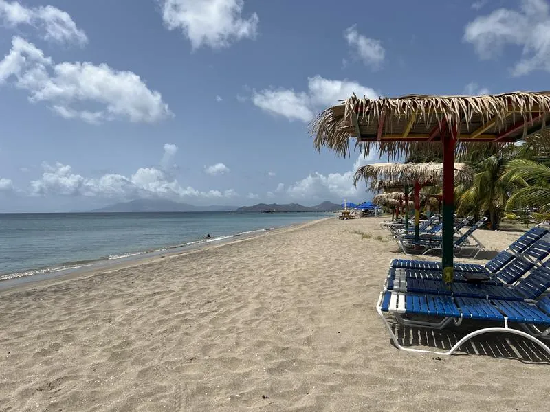 Pinney's Beach on Nevis, with a sandy shoreline, calm Caribbean water and palm trees beneath a partly cloudy sky.