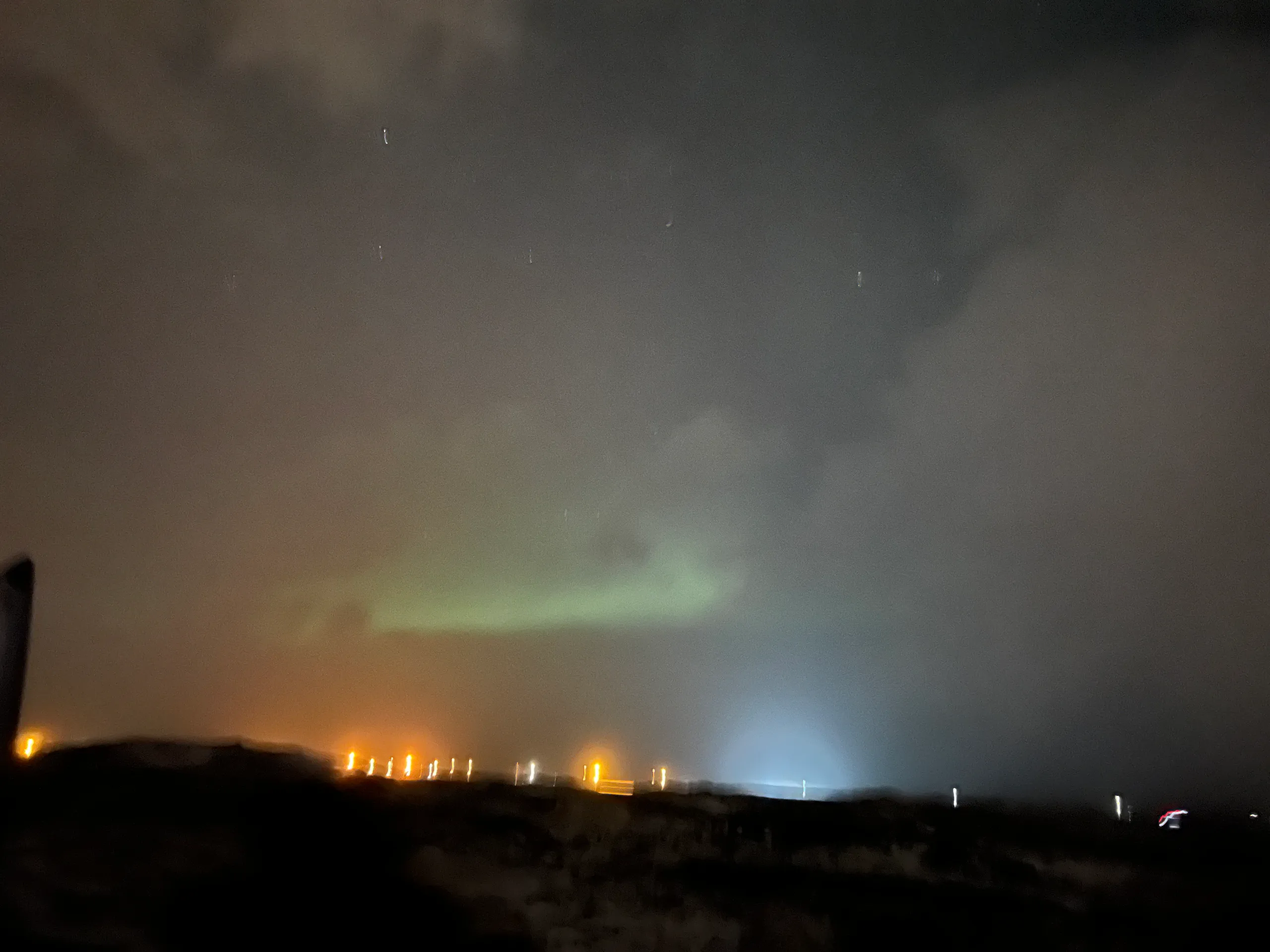 A green band of northern lights beneath cloud over an Icelandic night landscape.