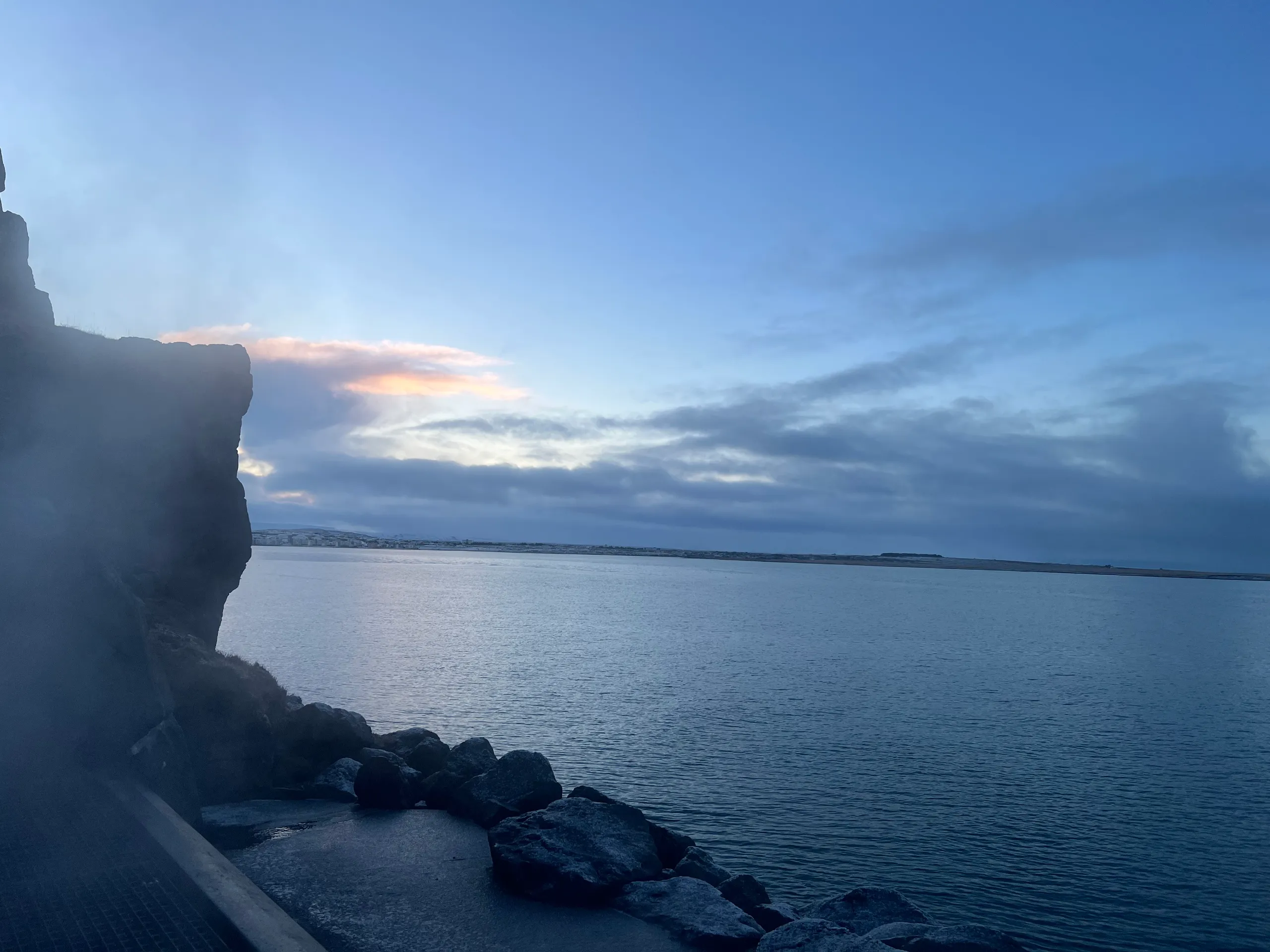 Steam rising beside dark rock and open water under a blue winter sky in Iceland.