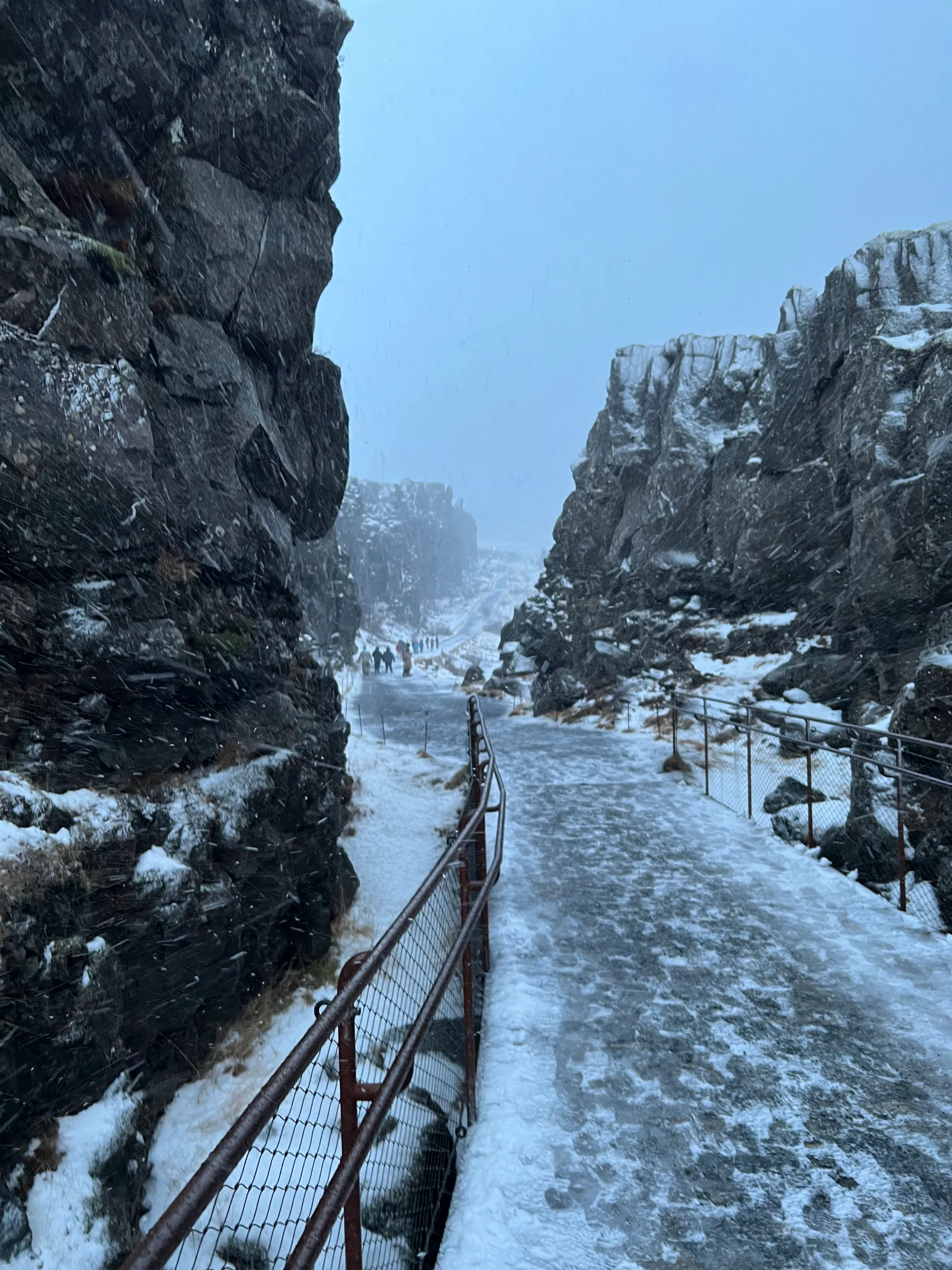 An icy path between dark rock walls at Þingvellir National Park during snowfall.