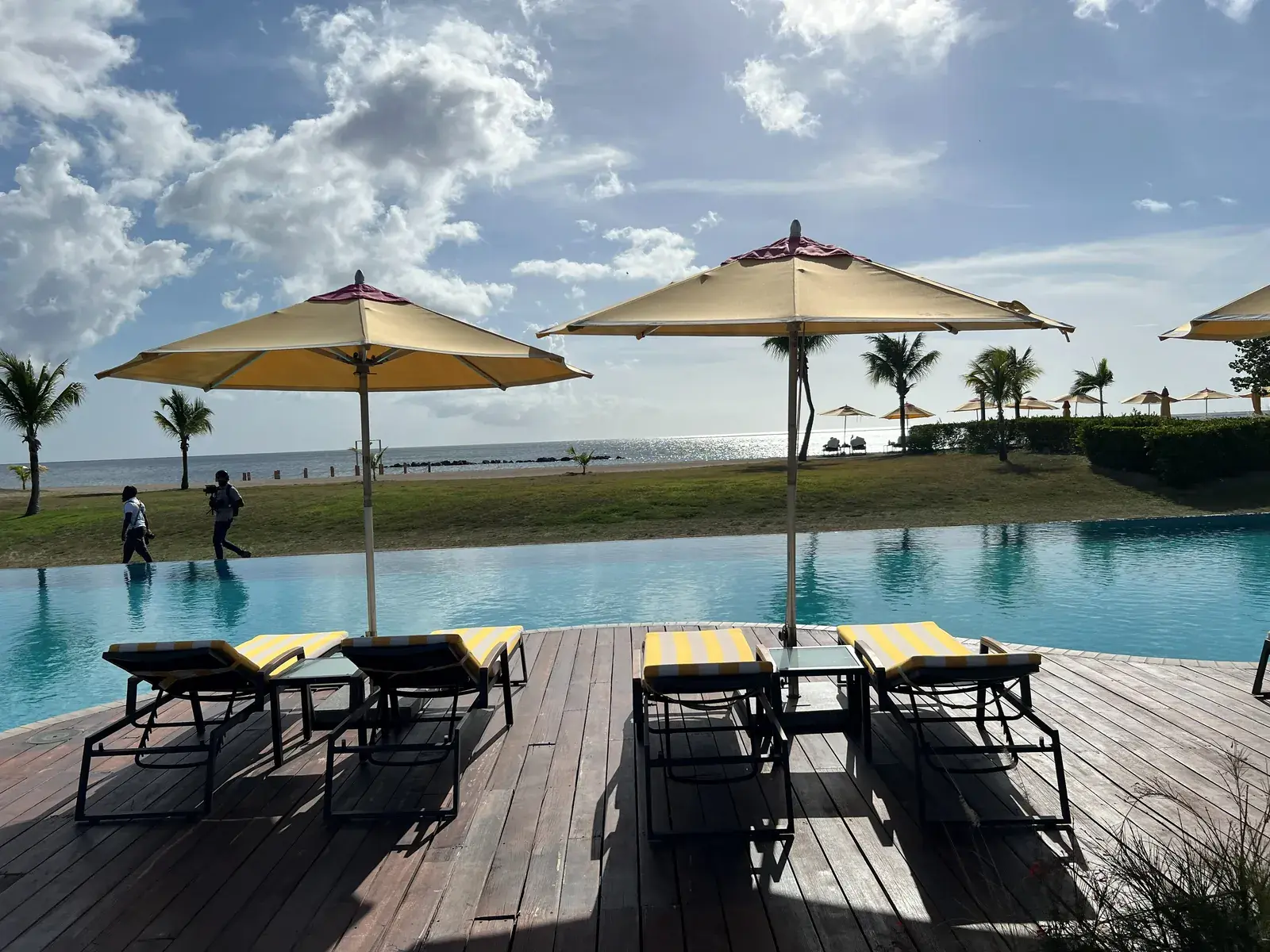 Striped loungers beneath umbrellas, a pool and the sea beyond a lawn.