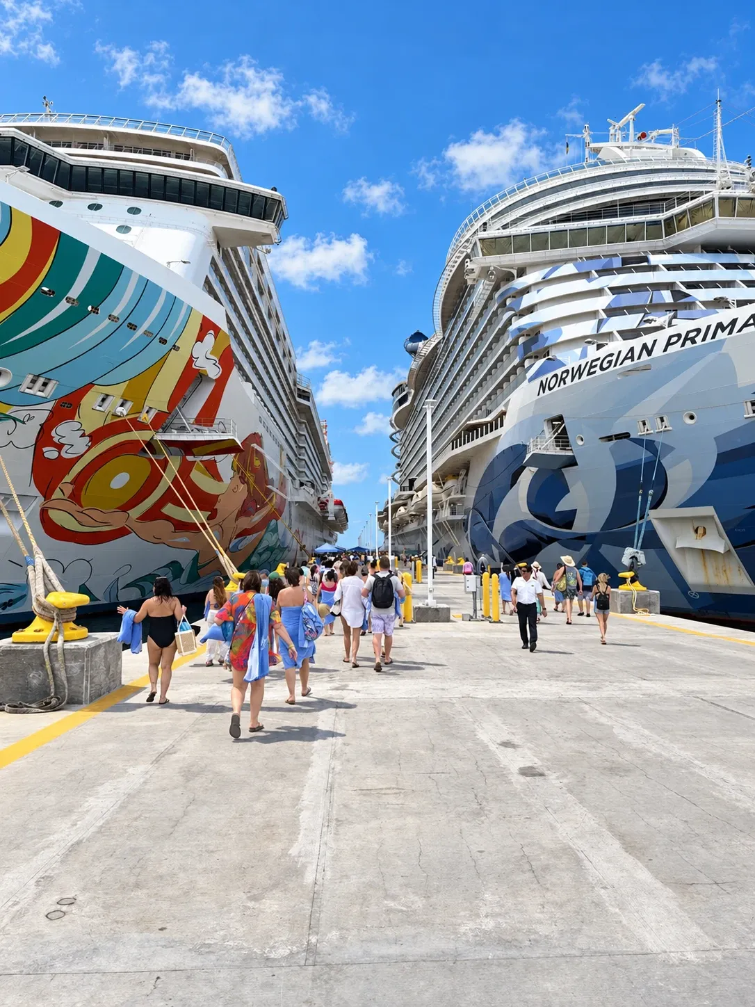 Passengers walking along the Great Stirrup Cay pier between Norwegian Getaway and Norwegian Prima under blue skies.
