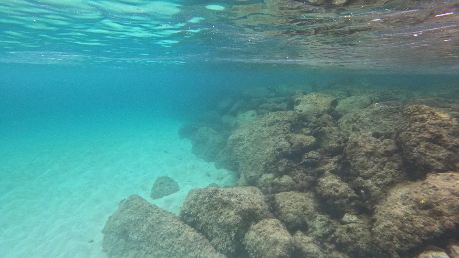 Sunlit submerged rocks and rippling surface reflections in clear turquoise water at Great Stirrup Cay.