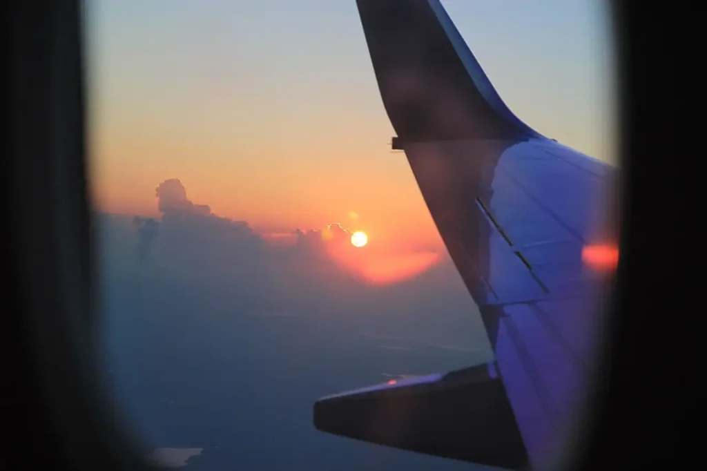 Airplane wing against a sunset seen through a cabin window