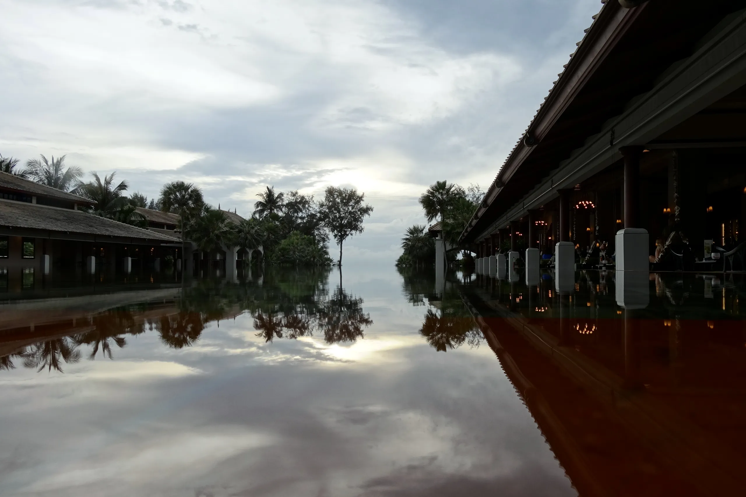 Palm trees and pavilion roofs reflected in still water at JW Marriott Phuket Resort & Spa.