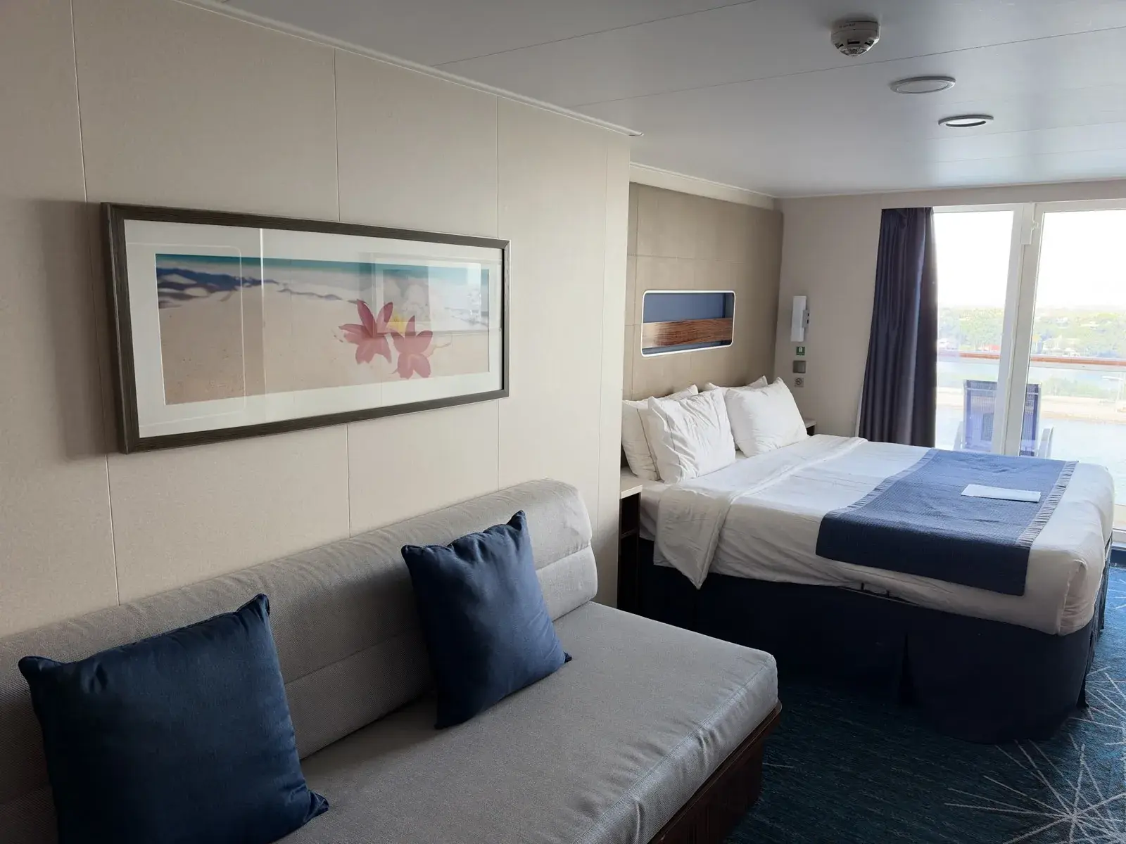 The Club Balcony Suite interior, with a sofa, bed, storage and balcony doors.