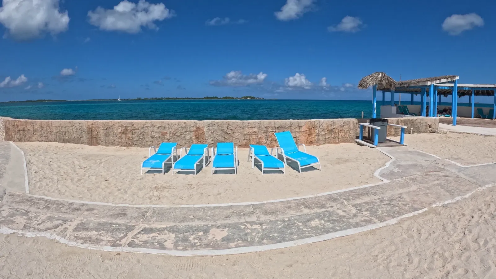 Empty blue loungers on the sand beside turquoise water and a beachfront pavilion at Pearl Island.
